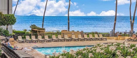 A poolside area with lounge chairs, a pool, and a view of the ocean.