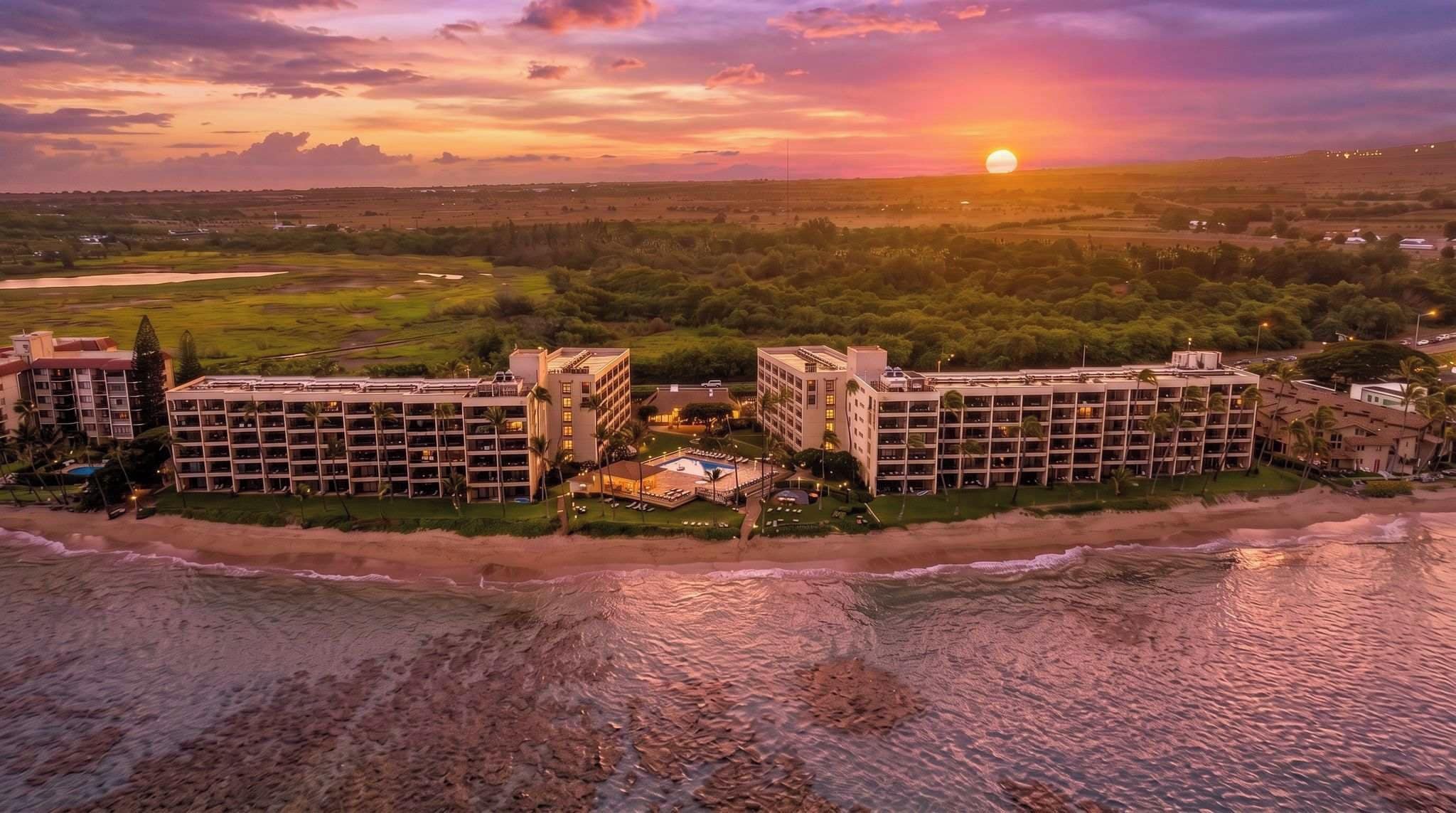 Un hotel frente al mar con varias edificaciones, piscina y vista al atardecer.