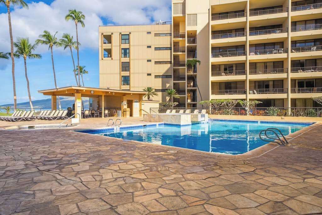 Un hotel con piscina, lettini, palme e vista sull'oceano.