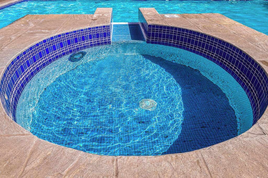 En rund pool med blå mosaikplattor och en kant av sten.