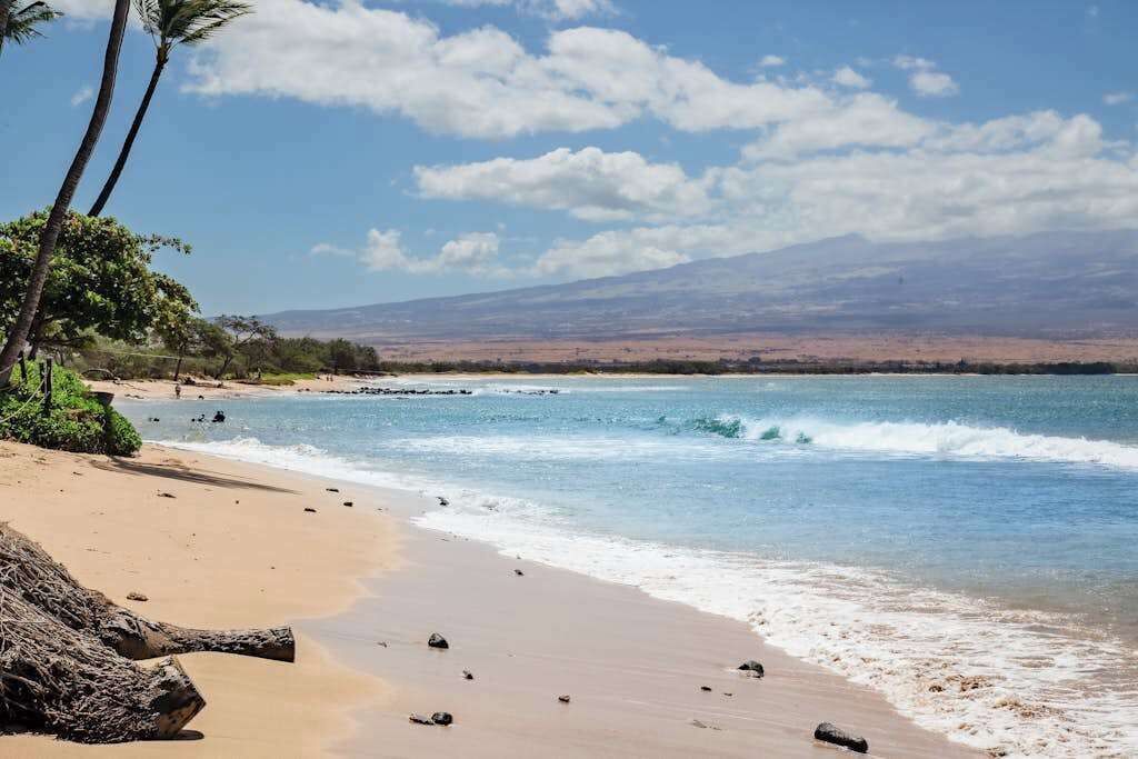Ein Strand mit blauem Himmel, ruhigem Wasser und Bergen in der Ferne.