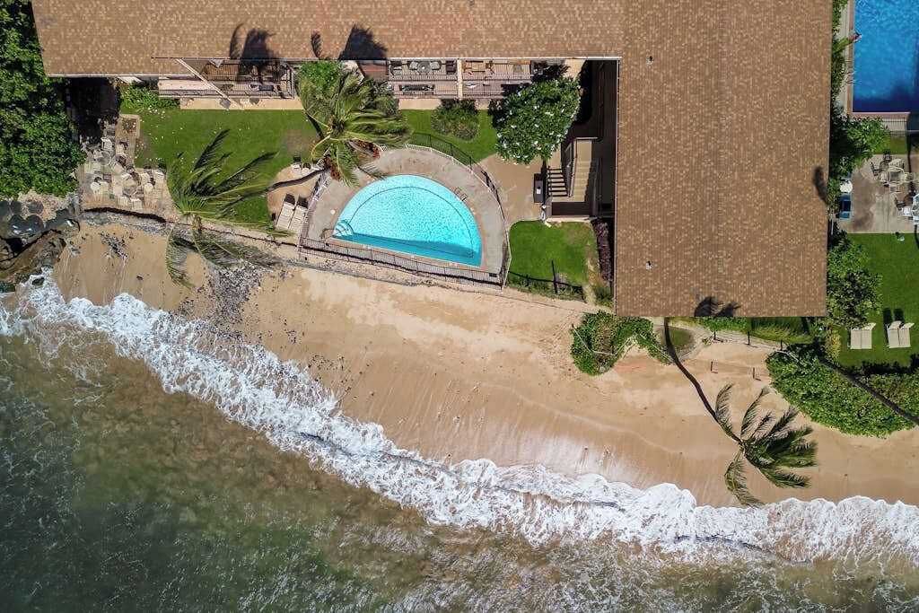 Vista aèria d'una propietat a primera línia de platja amb piscina, palmeres i sorra.