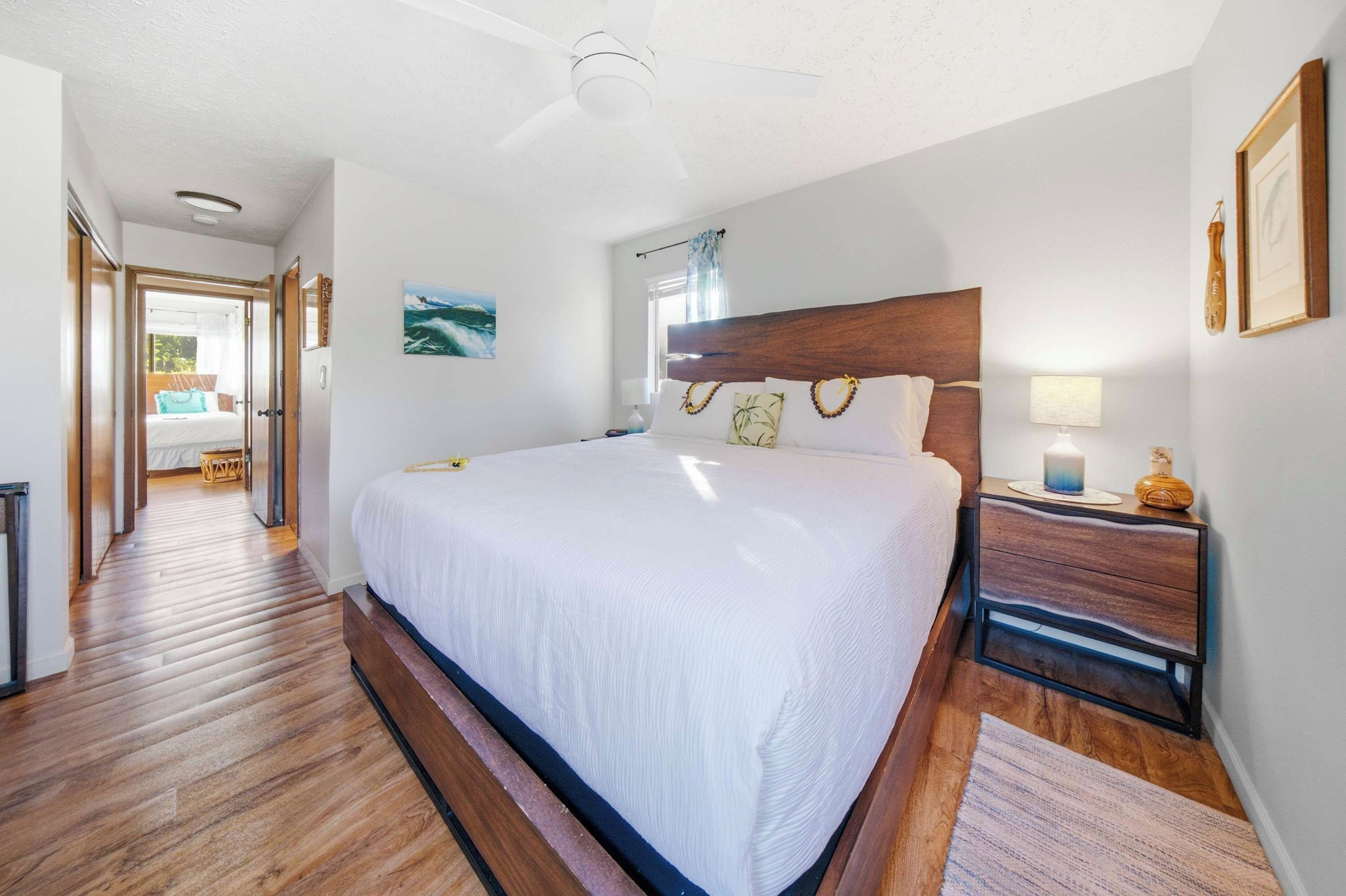 A hotel room with a large bed, wooden headboard, bedside tables, a nightstand, a ceiling fan, and a painting on the wall.