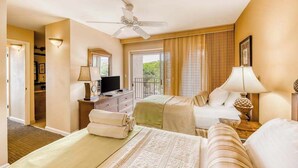 A hotel room with a bed, a desk with a television, a ceiling fan, and a balcony view.