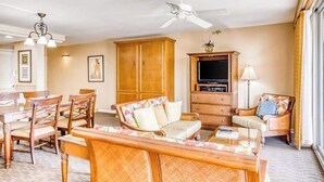 A living room with a sofa, chairs, a TV, a ceiling fan, and a dining area with a table and chairs.