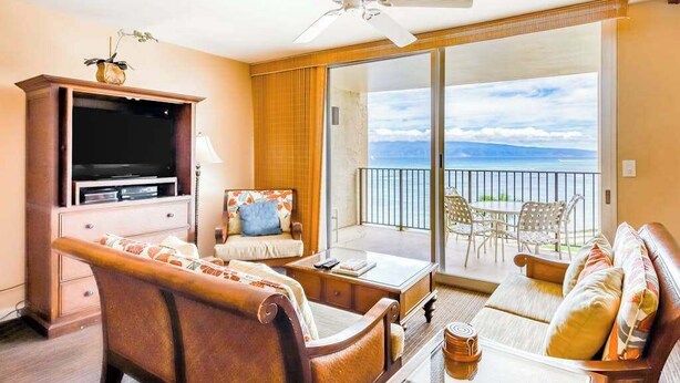 A room with a sofa, a television, a coffee table, and a balcony with a view.