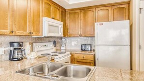 A kitchen with wooden cabinets, a white microwave, a white refrigerator, a stainless steel sink, a coffee maker, and a toaster.