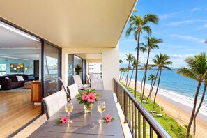 A balcony with a table set for dining, overlooking a beach with palm trees and the ocean. - *New* Two-Bedroom Ocean-View Sugar Beach Stay (Kihei)