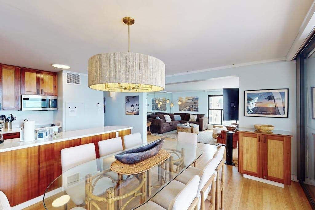 Une cuisine moderne dotée d’un îlot central, un coin repas avec une table en verre et un salon avec un canapé et un téléviseur.
