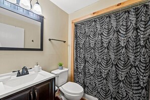 A bathroom with a white sink, dark cabinets, a white toilet, and a shower curtain with a leaf pattern. - Windy Oaks Condo (Gatlinburg)