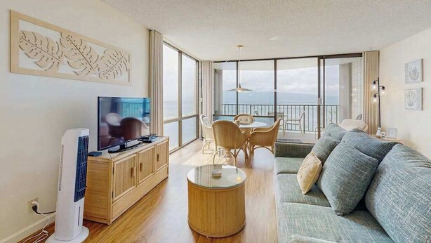 En moderne stue med et fladskærms-tv, træmøbler, et rundt sofabord og en balkon med udsigt.