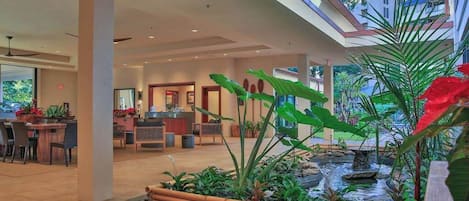 Un hall d’hôtel comprenant un comptoir d’accueil, un espace salon et un petit jardin intérieur agrémenté d’un élément aquatique.