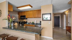 A kitchen with wooden cabinets, a granite countertop, and a built-in microwave. - *NEW* Fall $ale Ocean-View Kihei Escape Steps from The Cove (Kihei)