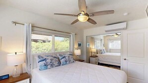 Ein Schlafzimmer mit einem Bett, Nachttischen, einem Deckenventilator, einem Fenster mit Vorhängen und einer Tür.