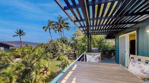 Eine Holzterrasse mit einer Pergola, einem Grill und Blick auf üppige tropische Vegetation.