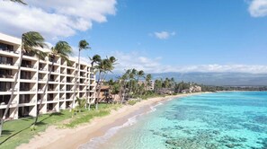 Un hôtel situé en bord de mer, avec plusieurs étages, une plage de sable et une eau turquoise cristalline.