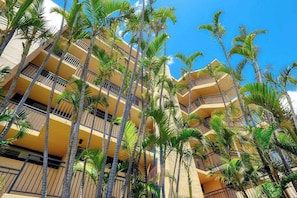 Ein mehrstöckiges Hotel mit Balkonen, Palmen und blauem Himmel.