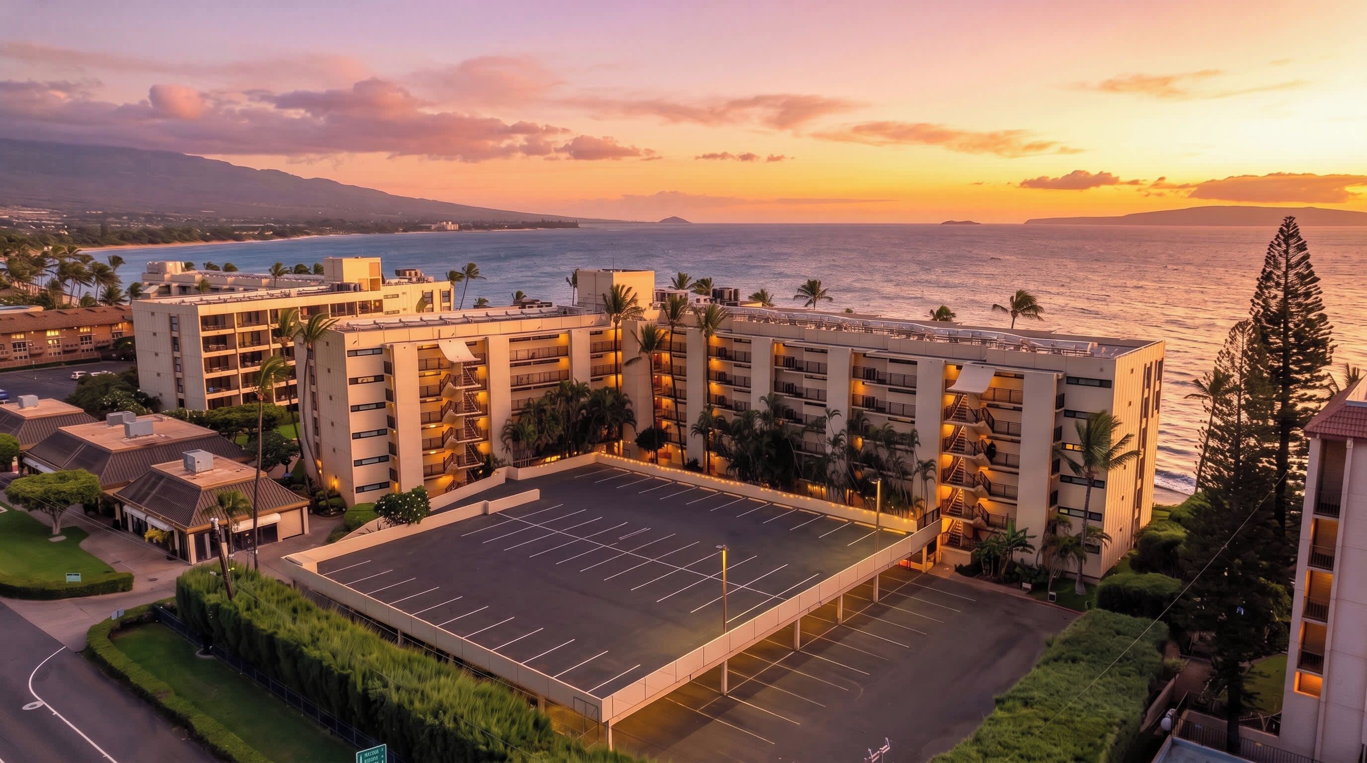 Un hotel con varios pisos, un estacionamiento y vista al océano al atardecer.