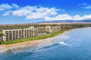 A beachfront hotel with multiple floors, a sandy beach, and a view of the ocean and distant hills. - NEW Garden-View 1BR Sugar Beach Resort Condo for Four (Kihei)
