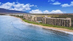 Un hotel frente al mar con varias construcciones, una playa y montañas al fondo.