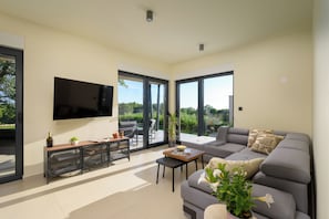 A modern living room with a grey sofa, a flat-screen TV, and a dining area with a table and chairs. - Villa Casa Luta (Istria - Tinjan) (Tinjan)