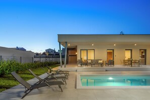 Ein moderner Außenpoolbereich mit Liegestühlen, einem Esstisch und einer überdachten Terrasse.