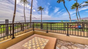 A balcony with a checkered floor, palm trees, and a view of the beach. - NEW Oceanfront Comfort for Four at Sugar Beach (Kihei)