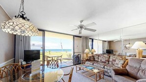 A hotel room with a balcony, a dining area with a glass table, a sofa, and a television. - NEW Oceanfront Comfort for Four at Sugar Beach (Kihei)