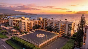 Um hotel com vários andares, uma piscina no terraço e vista para o oceano ao pôr do sol.
