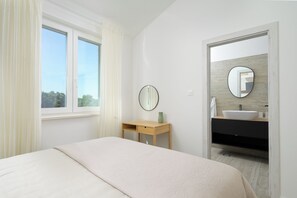 Une chambre à coucher comprenant un lit, une table de chevet et un miroir, ainsi qu’une salle de bain avec un lavabo et un miroir.