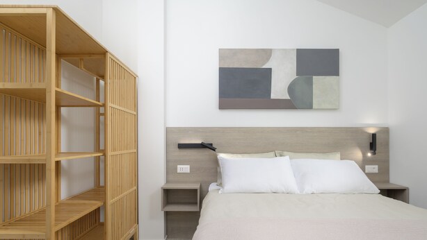 Quarto com cama, estante de madeira e pintura abstrata na parede.