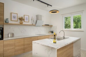 Eine moderne Küche mit Marmorarbeitsplatten, Holzschränken, einem Einbauofen, einem Spülbecken und einem Fenster mit Blick ins Grüne.