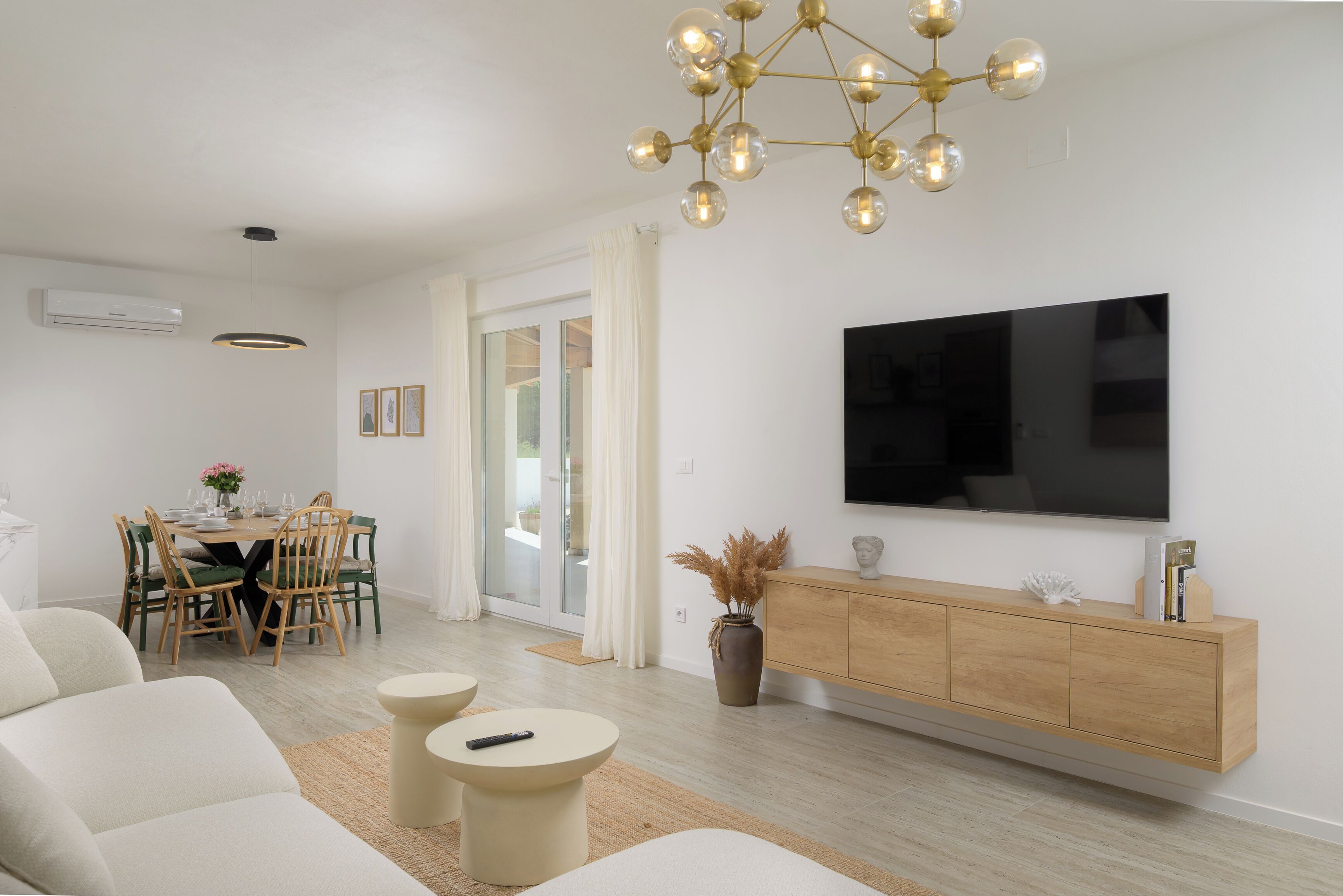 A modern living room with a flat-screen TV, a dining area with a table and chairs, and a sofa.