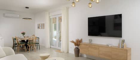 A modern living room with a flat-screen TV, a dining area with a table and chairs, and a sofa.