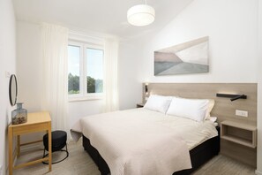 Ein Schlafzimmer mit einem Bett, einem Nachttisch, Vorhängen an einem Fenster und einem Wandbild.