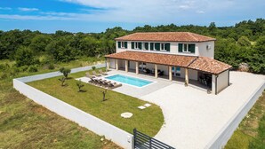 Uma casa de dois andares com piscina, rodeada por vegetação e um céu claro.