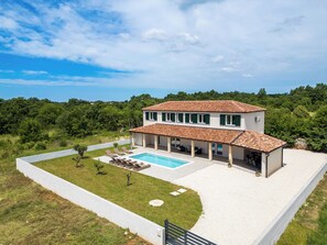 Ein zweistöckiges Haus mit Swimmingpool, umgeben von Grünflächen und blauem Himmel.