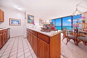 Una cucina con mobili in legno, pavimento piastrellato e zona pranzo con vista sull'oceano.