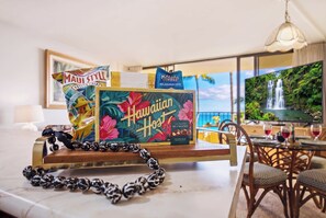 Habitació d'hotel amb vista a una cascada, una taula amb una ampolla de Kauai Coffee, un paquet de Patates Portatlatch tipus Maui, i un collar de boles.
