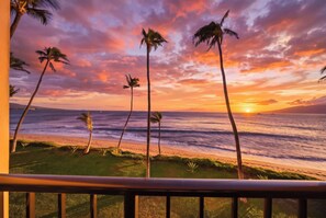 Tramonto visto da un balcone con vista su una spiaggia, palme e l'oceano.