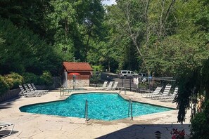 Una piscina con sillas de descanso, un edificio pequeño y un área cercada con un vehículo.