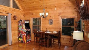 A wooden interior with a dining table, chairs, a chandelier, and a video game console. - Yeti Lodge (Gatlinburg)