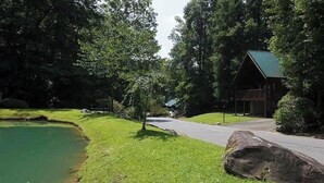 A cabin with a green roof, surrounded by a pond and lush greenery. - Yeti Lodge (Gatlinburg)