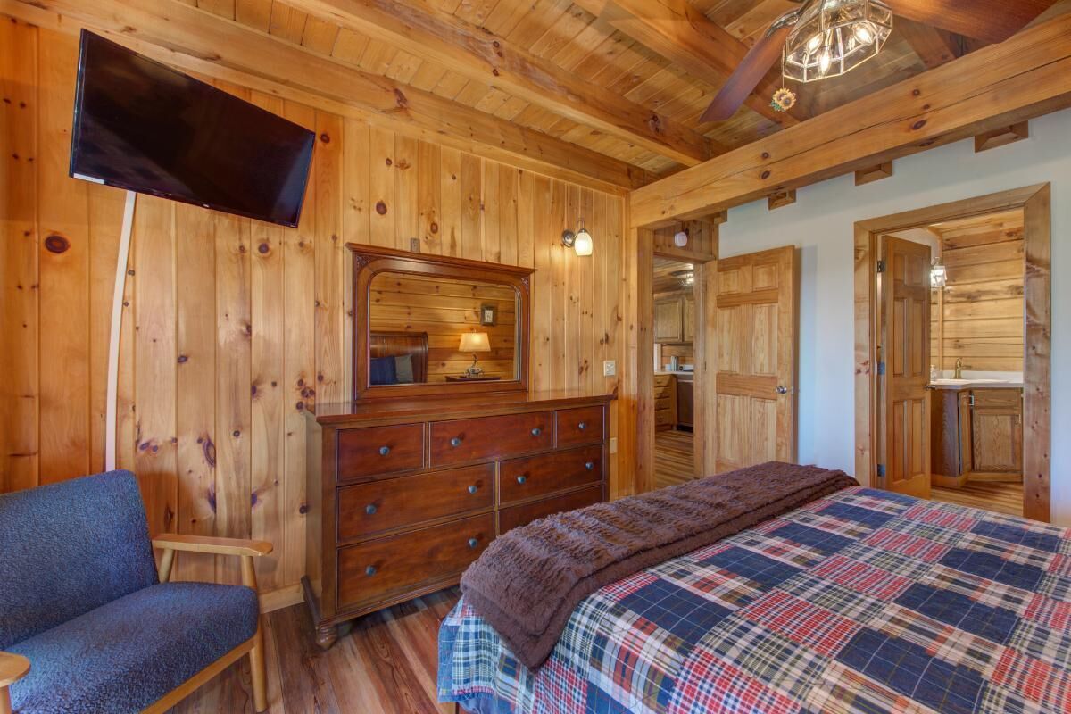 A wooden-paneled room with a bed, dresser, and a television mounted on the wall.