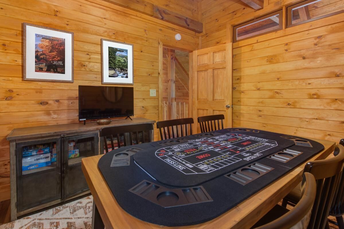 A wooden cabin interior with a poker table, framed pictures on the wall, and a television.