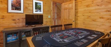 A wooden cabin interior with a poker table, framed pictures on the wall, and a television.