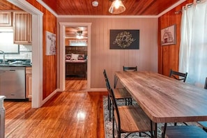 A dining area with a wooden table and chairs, a kitchen in the background, and a hallway leading to a bedroom. - Gatlinburg's Cozy Rose (Gatlinburg)