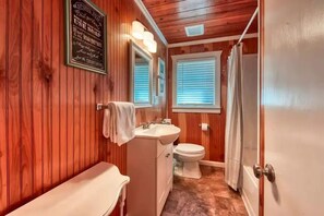 A wooden-paneled bathroom with a sink, toilet, and a shower curtain. - Gatlinburg's Cozy Rose (Gatlinburg)