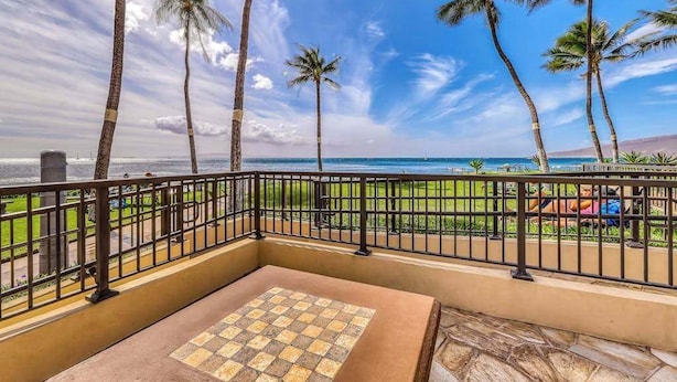 Un balcón con piso a cuadros, palmeras y vista a la playa.