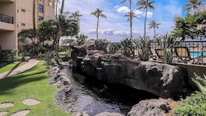 Zona ajardinada con una formación rocosa, palmeras y una piscina.